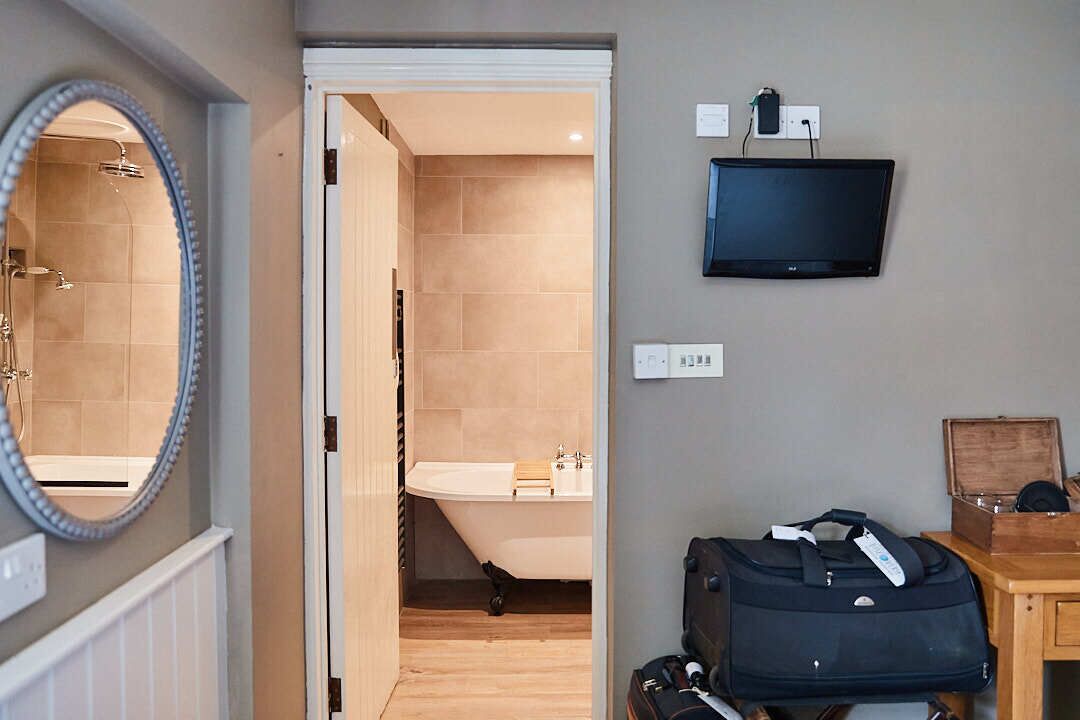 A bathroom with a bathtub, a mirror, a television, and a wooden desk with a suitcase.