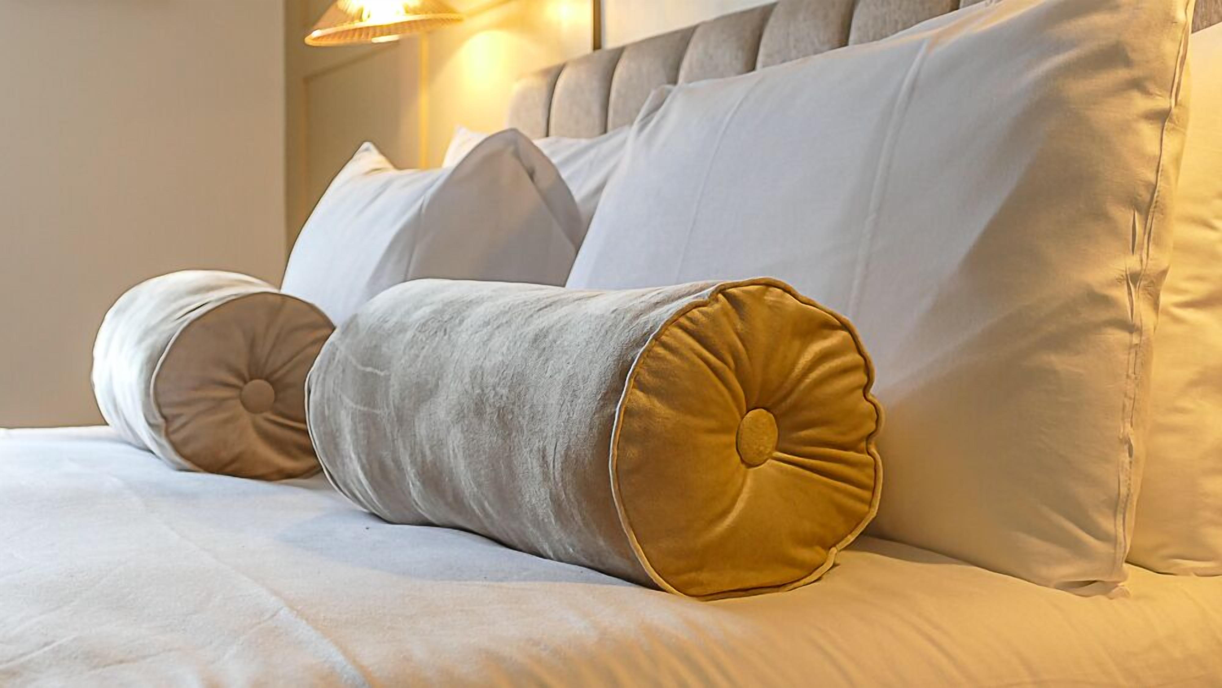 Un lit avec du linge de lit blanc et deux oreillers, dont l’un est agrémenté d’un motif doré.