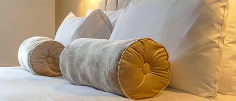 Un lit avec du linge de lit blanc et deux oreillers, dont l’un est agrémenté d’un motif doré.