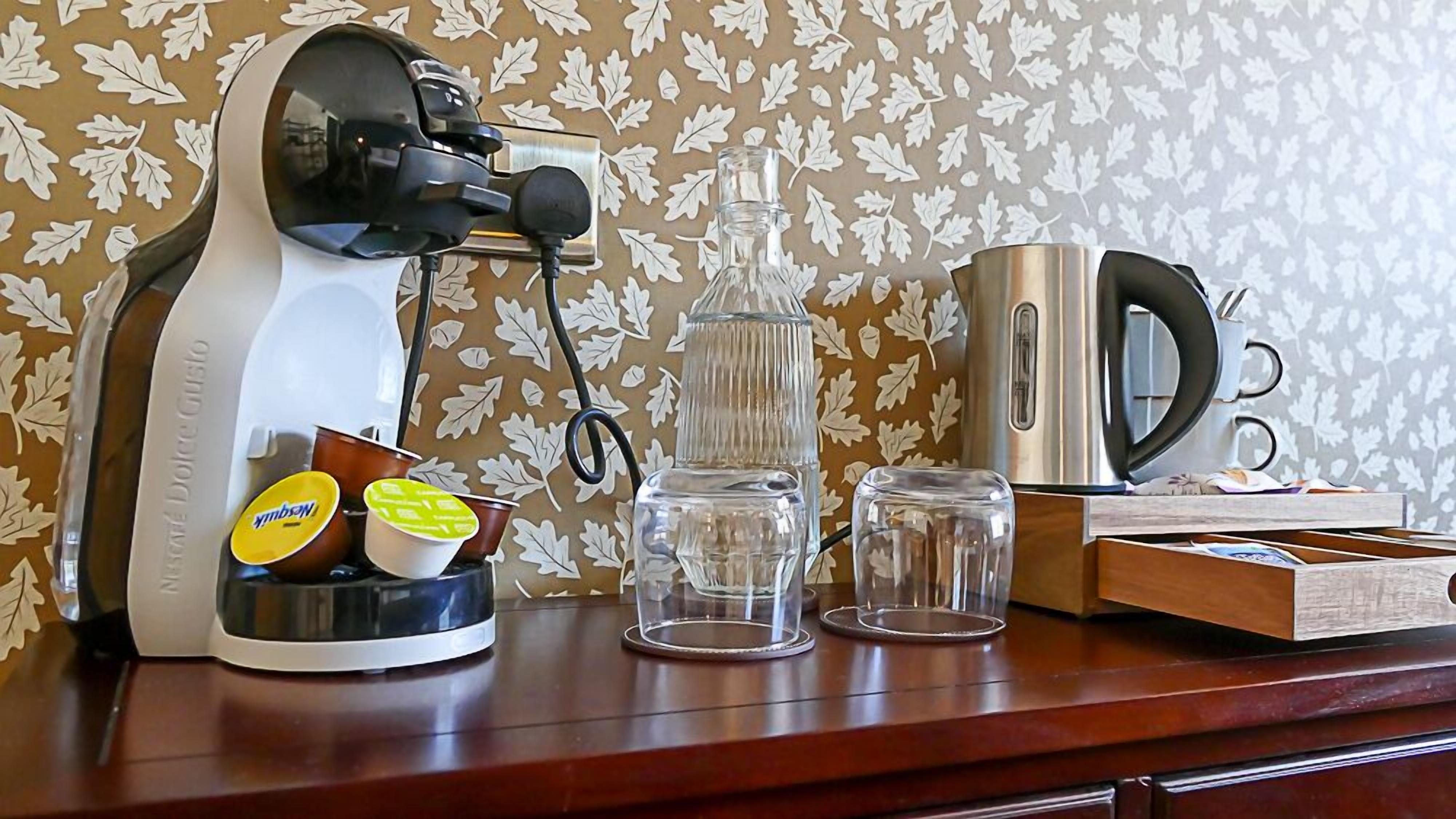 A kitchen counter with a coffee maker, a glass carafe, a coffee pot, and a box of coffee pods.