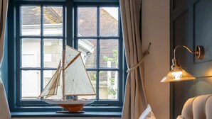 A bedroom with a bed, a window with curtains, a radiator, and a lamp. - The Bugle Coaching Inn (Yarmouth)