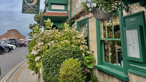 A traditional building with a green facade, a sign for 'The Bugle Coaching Inn', and a stone wall with flowers. - The Bugle Coaching Inn (Yarmouth)