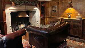 A cozy living room with a fireplace, leather sofa, and a wooden cabinet with a vintage lamp. - The Bugle Coaching Inn (Yarmouth)