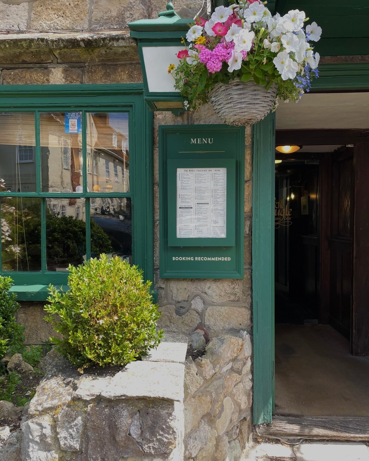 A stone building with a green door labeled "MENU" and a flower basket above it.