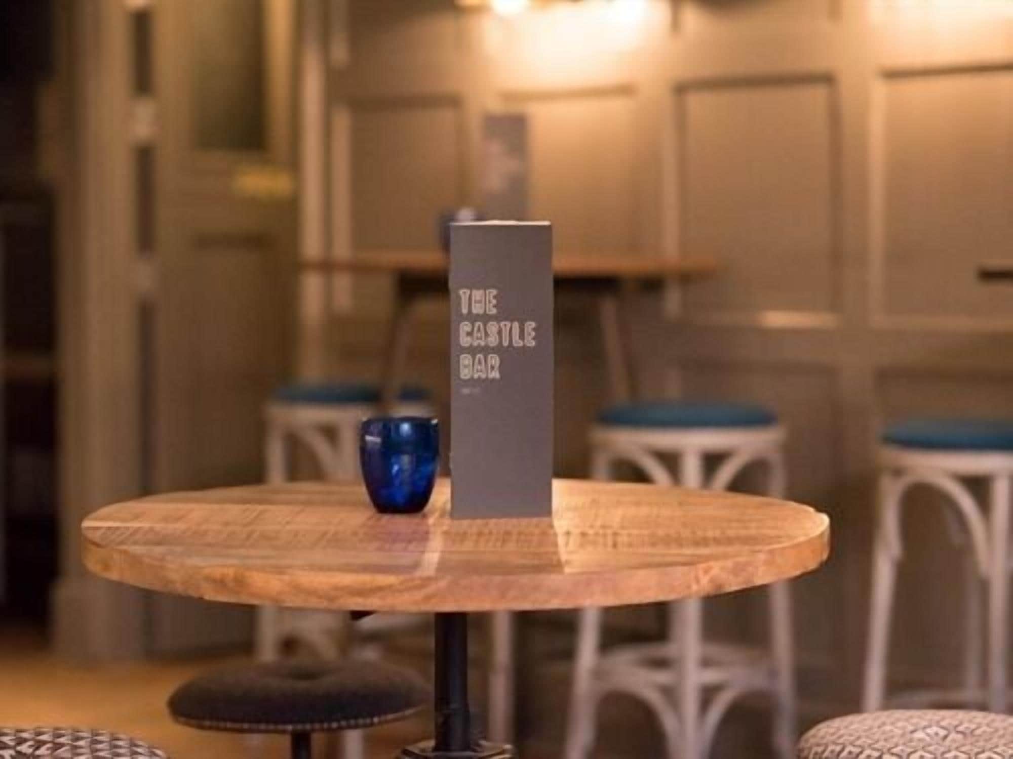 A round wooden table with a sign reading "THE CASTLE BAR" in a room with white furniture and a warm ambiance.
