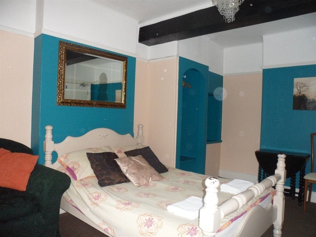 A bedroom with a bed, a mirror, a door, and a small table.