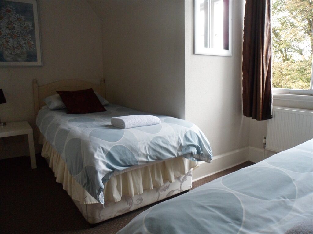 A bedroom with a bed, a nightstand, a window with curtains, and a painting on the wall.
