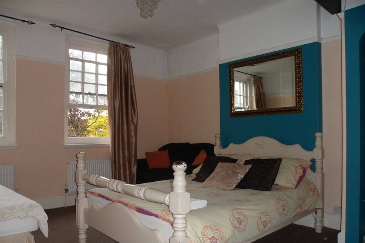 Un dormitorio con cama, ventana con cortinas, espejo y radiador.