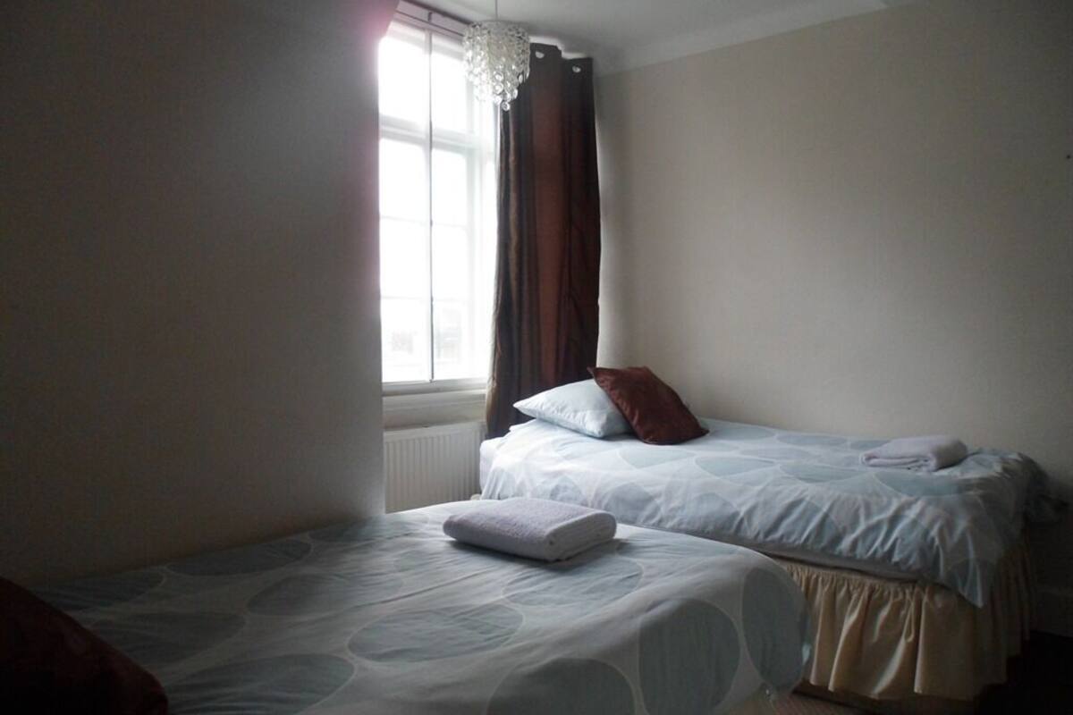 Una habitación con dos camas, una ventana con cortinas y un candelabro.