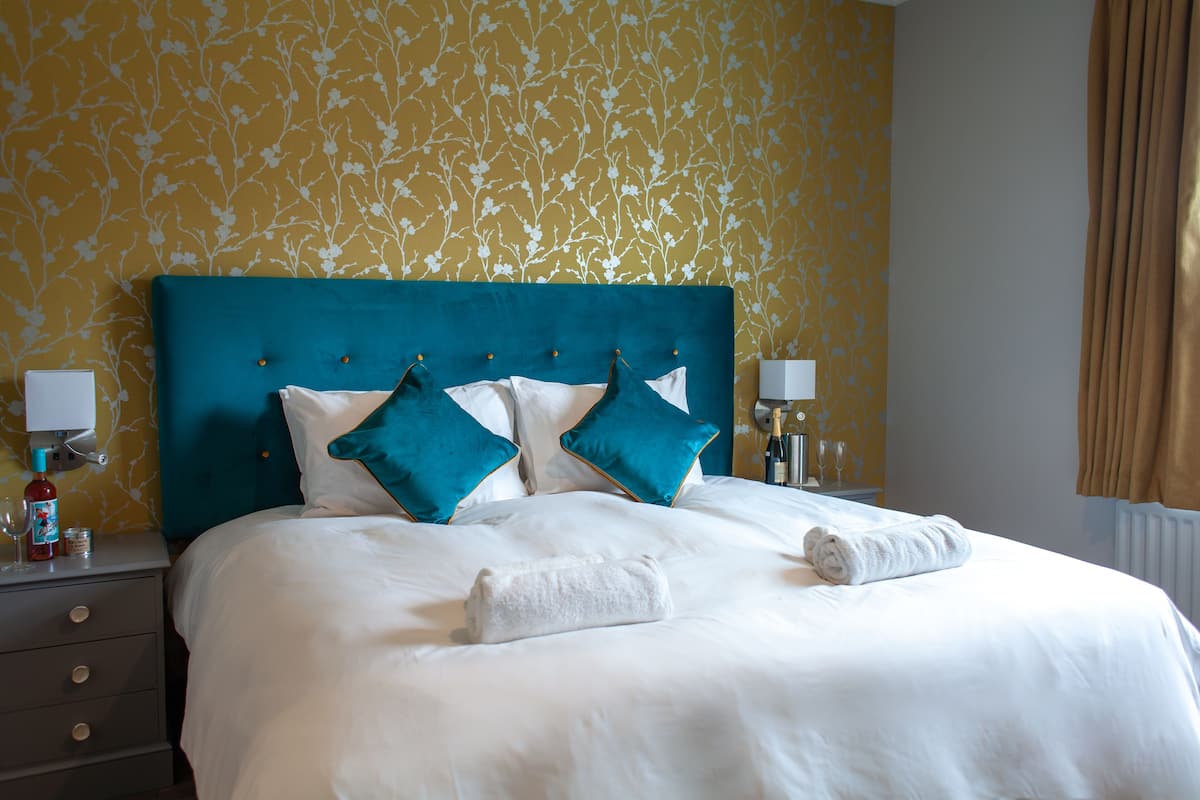 A neatly made bed with white bedding and teal pillows, a blue headboard, and two bedside lamps.