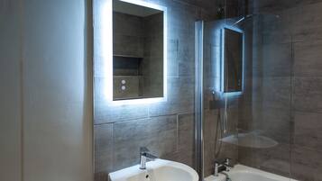 Een moderne badkamer met een glazen douchecabine, een witte wastafel en een spiegel met ingebouwde verlichting.