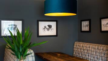 A restaurant interior with a wooden table, a cushioned bench, framed artwork on the wall, and a blue hanging light fixture.