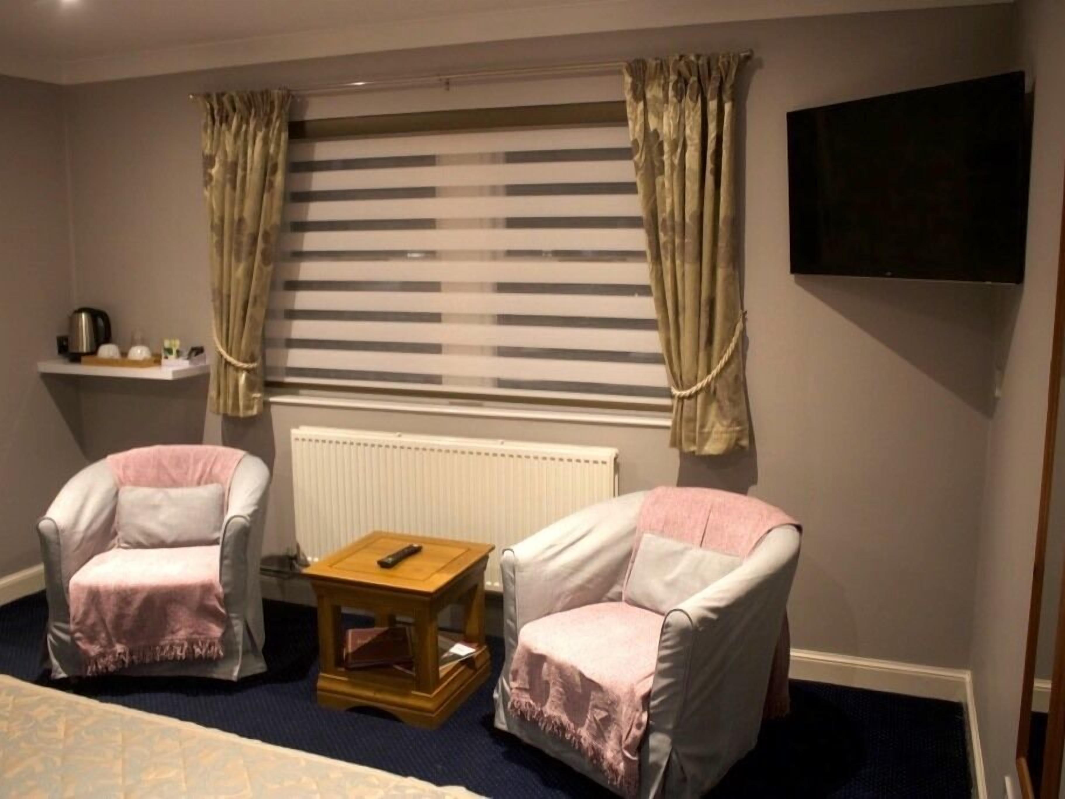 A room with two armchairs, a small wooden table, a radiator, and a TV mounted on the wall.