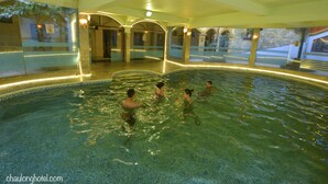 Une piscine intérieure à l’eau claire, entourée d’une terrasse carrelée et dotée de murs en verre.