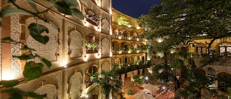 A multi-story building with balconies, a courtyard with palm trees, and a sign that reads "Hotel".