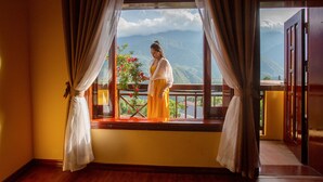 Une pièce avec un balcon, une vue sur les montagnes, et une personne debout près de la fenêtre.