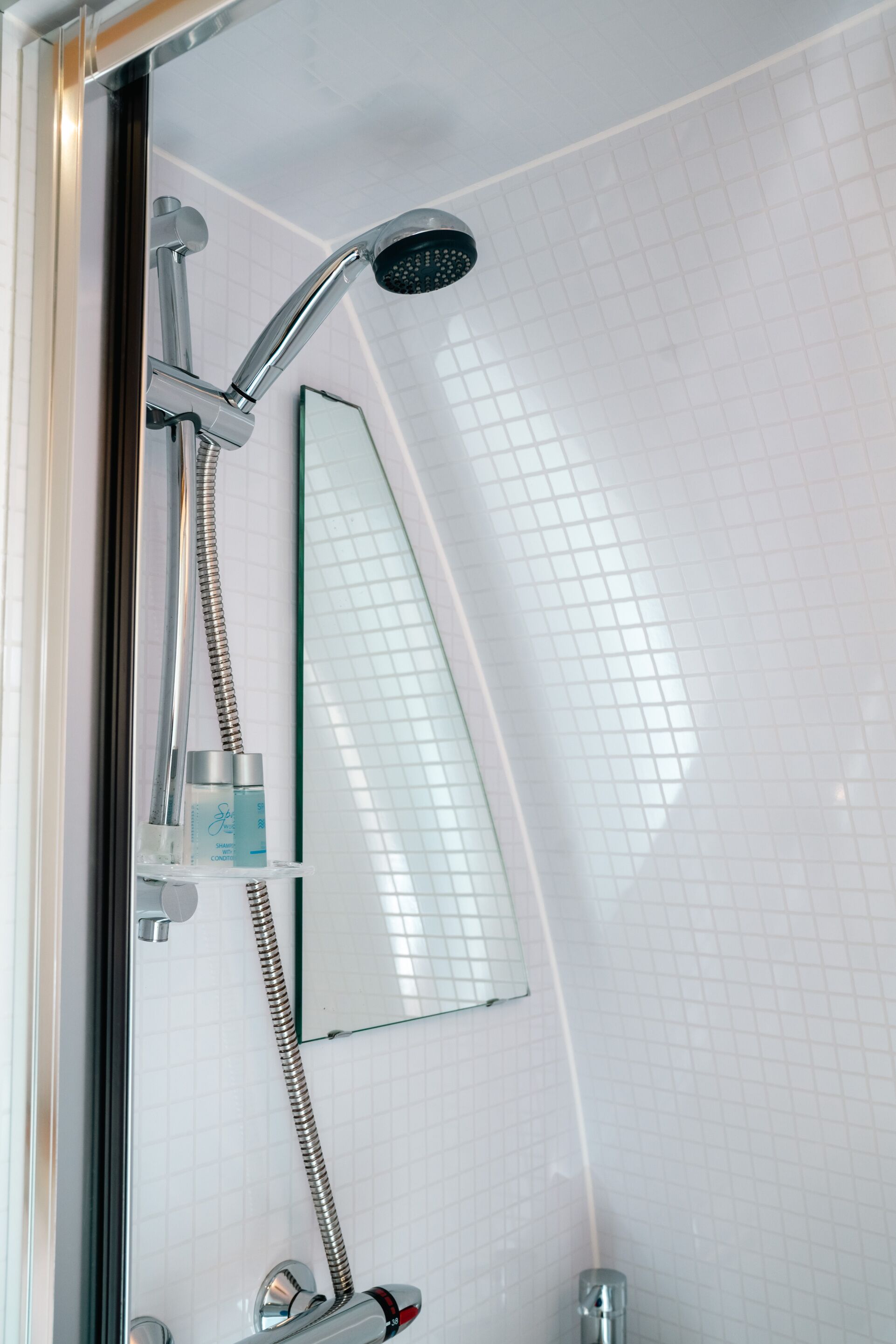 Une douche équipée d’un pommeau de douche à main et d’un robinet fixé au mur.