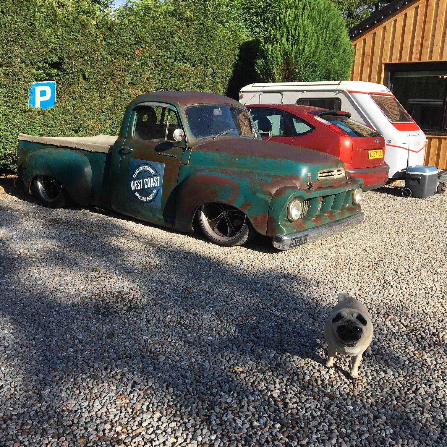 A vintage pickup truck with a West Coast Custom decal parked on gravel.