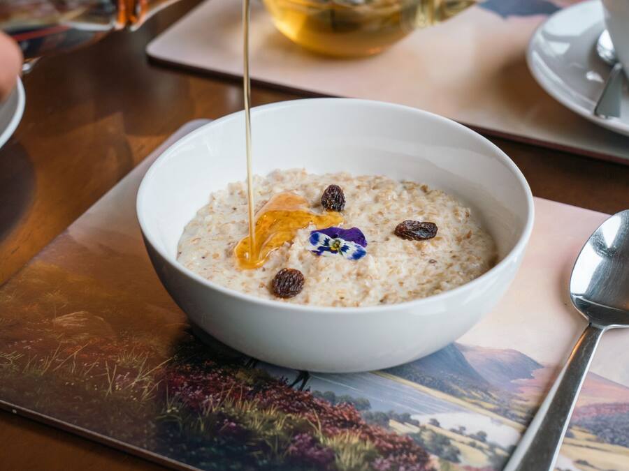 Een kom havermout met honing en rozijnen op een tafel met een theepot en kopjes.