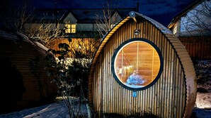 Una estructura de madera circular con un ventanal grande, rodeada de nieve y un cielo oscuro.