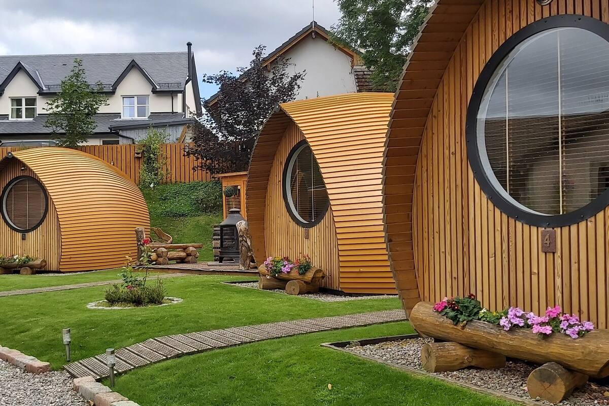 Eine Reihe von holzverkleideten, kuppelartigen Hütten mit großen Fenstern, angeordnet in einem Garten mit gepflegtem Rasen und Blumenbeeten.