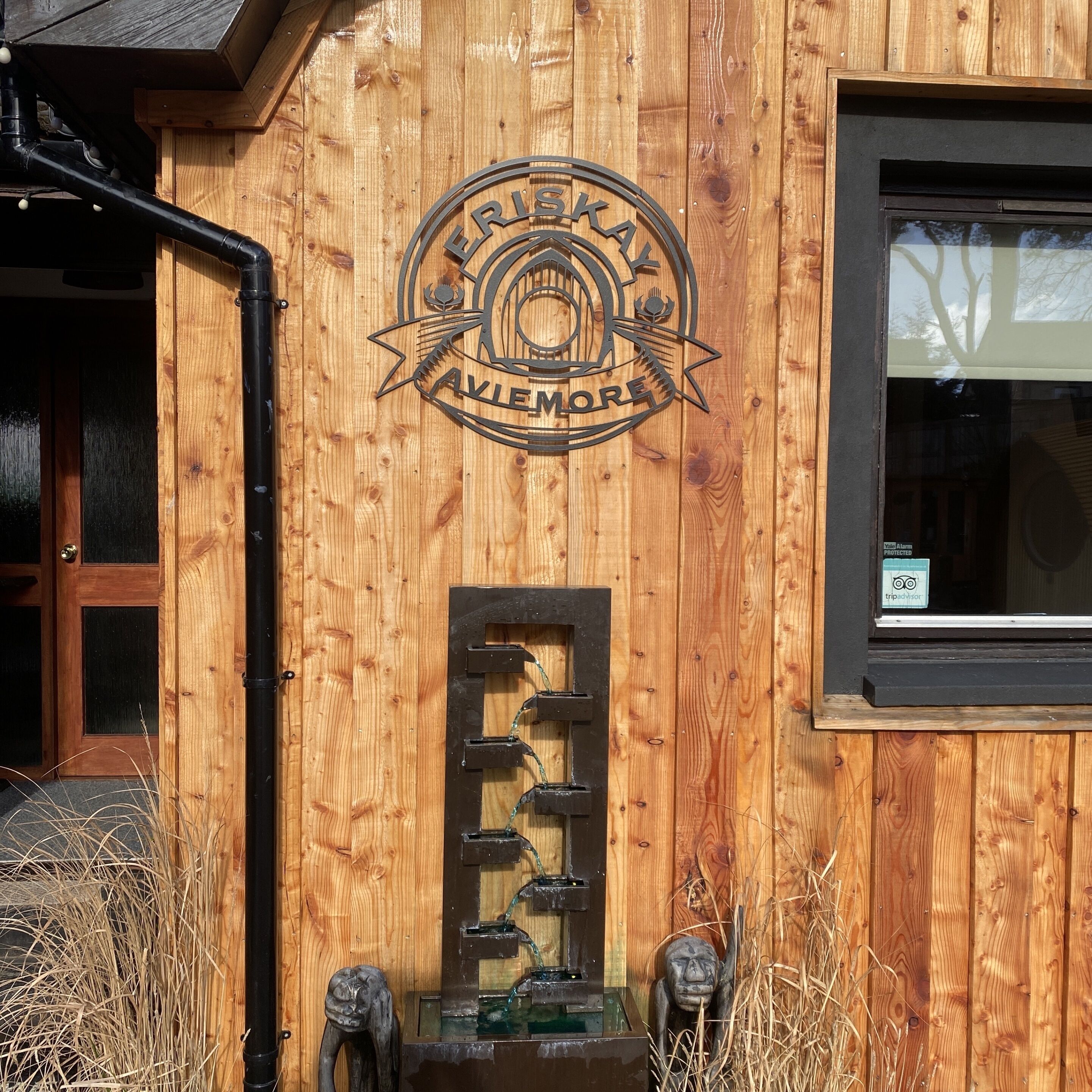 A wooden building with a circular emblem reading "ERISKAY AVIENMORE" and a window with a view of trees.