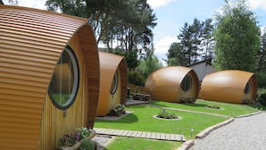 Una hilera de cabañas cilíndricas de madera con ventanas amplias, rodeadas de un césped cuidado y senderos de grava.