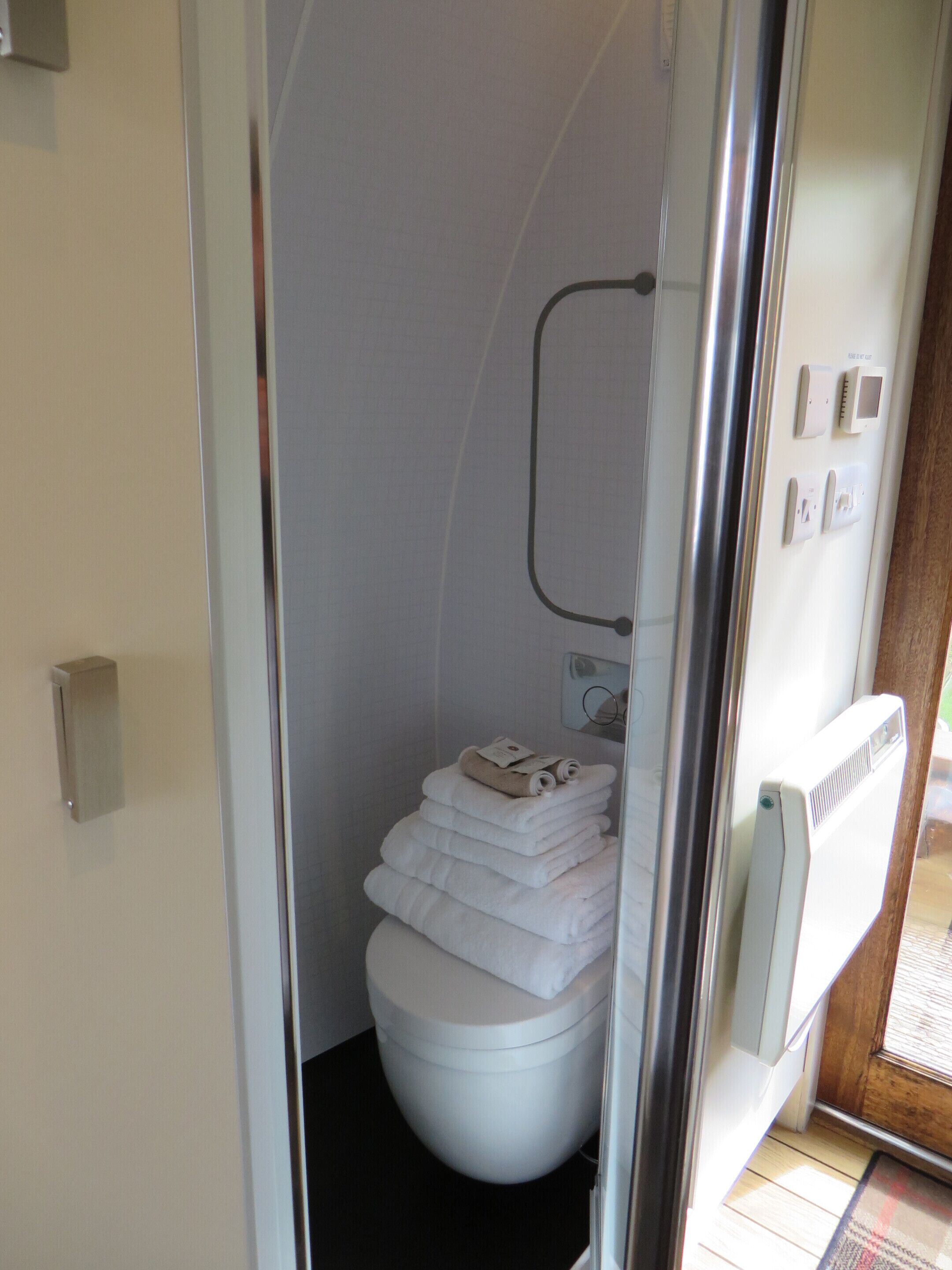 A compact, modern bathroom with a white toilet, a glass shower enclosure, and neatly stacked towels.