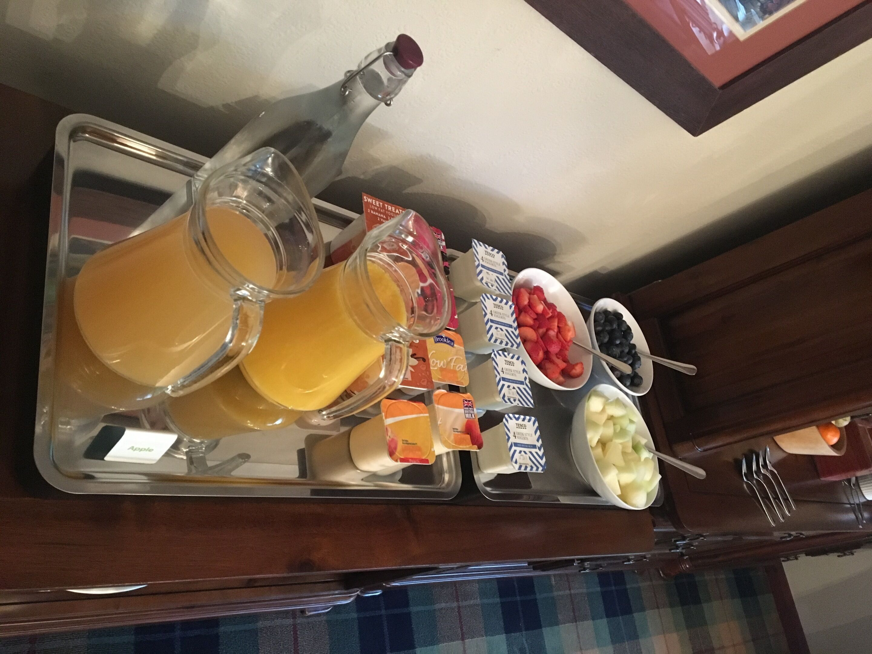 A tray with a bottle of orange juice, a pitcher, and various fruits including strawberries, blueberries, and apples.