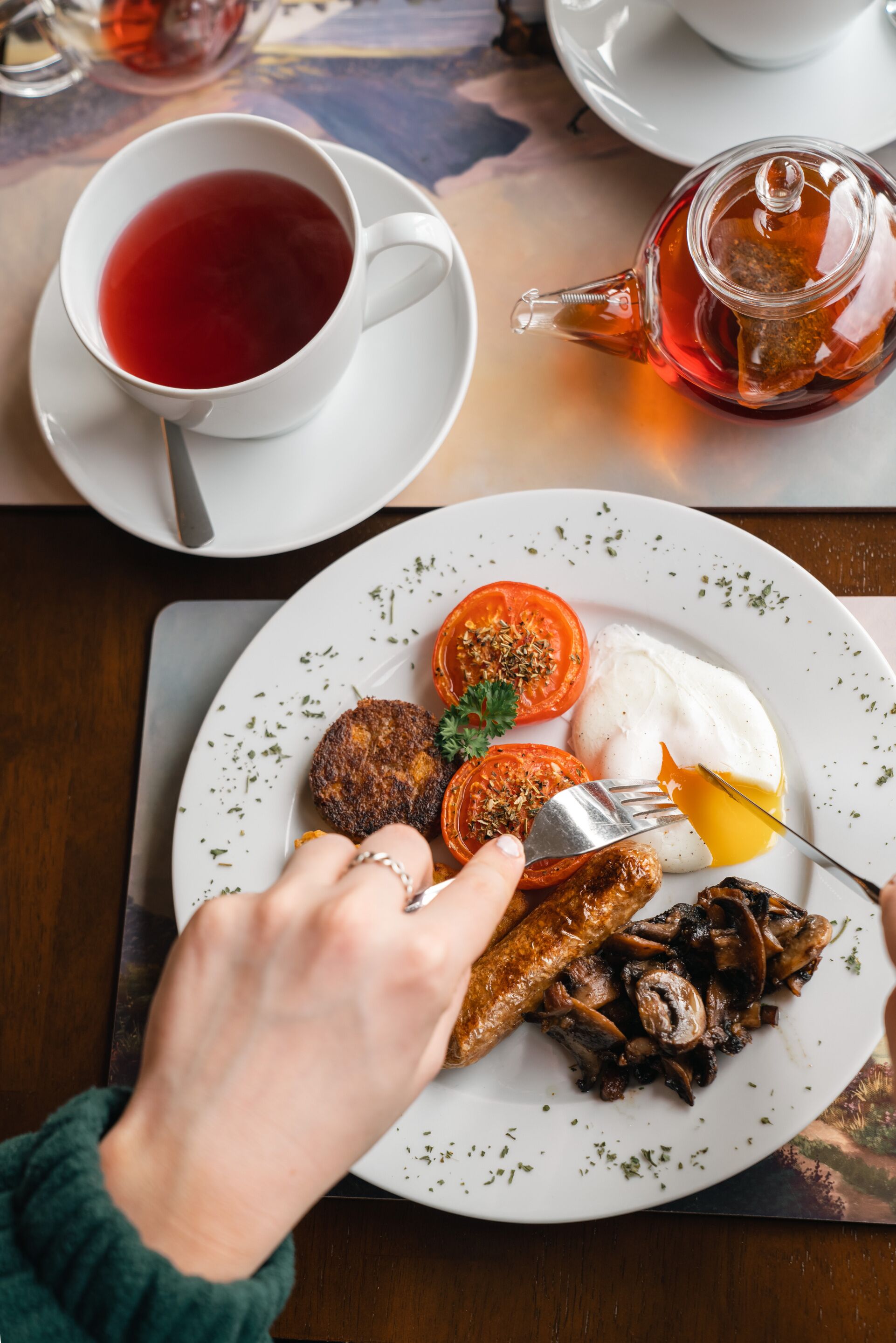 A dining table with a plate of food, a cup of tea, and a teapot.