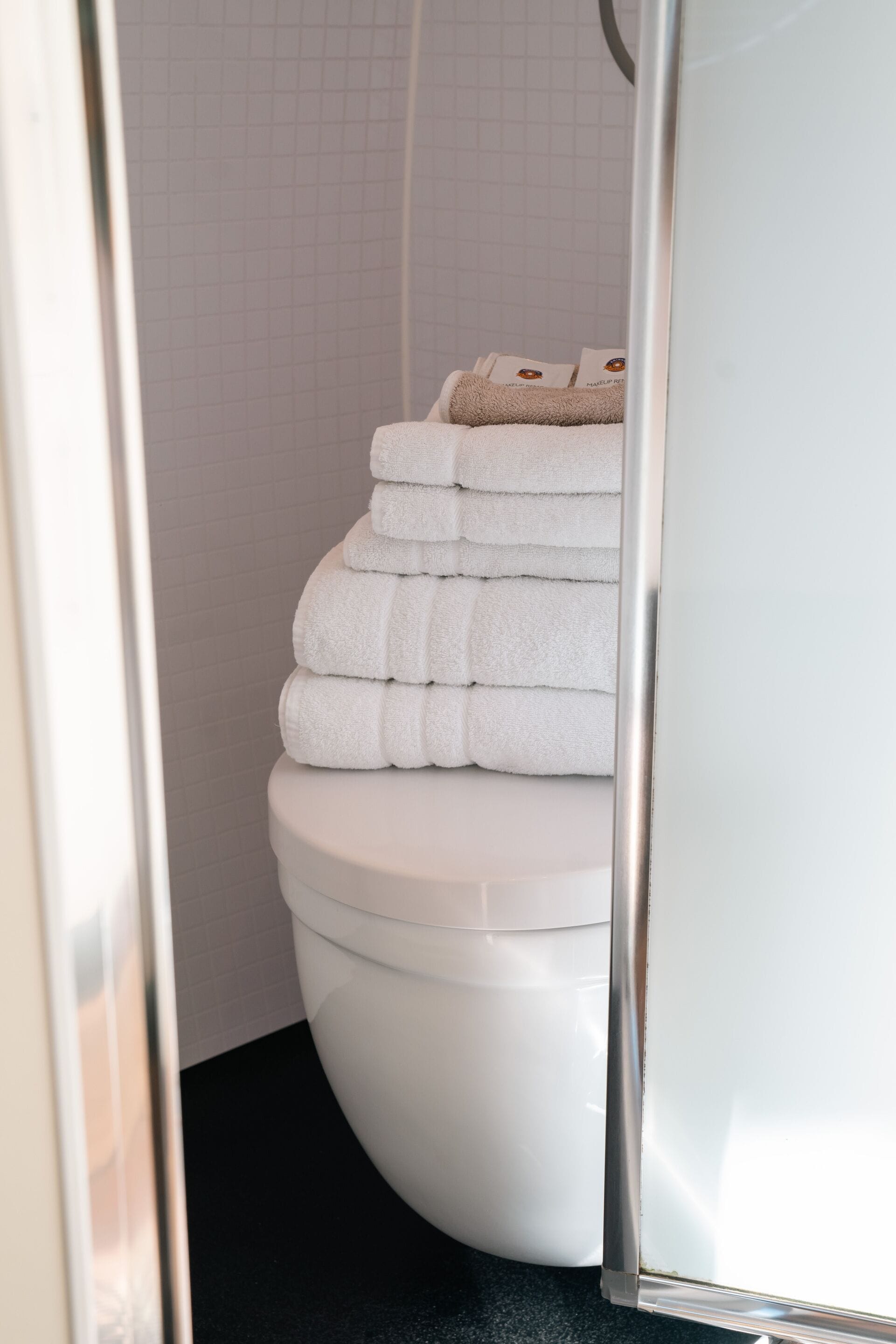 A bathroom with a white toilet, a stack of white towels, and a shower area.