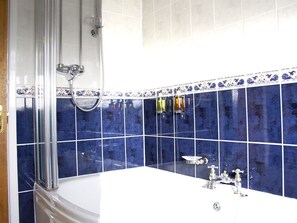 A bathroom with a white bathtub, a glass-enclosed shower, and blue-tiled walls.