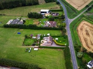 An aerial view of a rural area with a main road, a large open field, and several houses with varying roof styles.