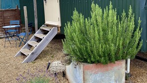 A small building with a door and windows, a wooden staircase leading to the door, and a large planter with green plants. - Fourwinds Leisure (March)