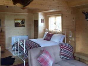 A cabin with two beds, a sofa, a painting, and a window with blinds.