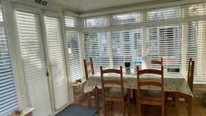A dining area with a table set for four, surrounded by wooden chairs, with a view through white blinds. - Fourwinds Leisure (March)