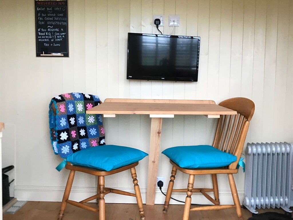 A small room with a wooden table and two chairs, a television mounted on the wall, and a radiator.