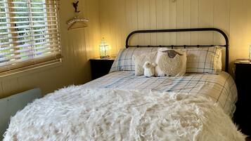 A cozy bedroom with a bed, a nightstand, a window with blinds, and a decorative wall piece.