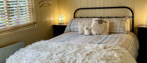 A cozy bedroom with a bed, a nightstand, a window with blinds, and a decorative wall piece.