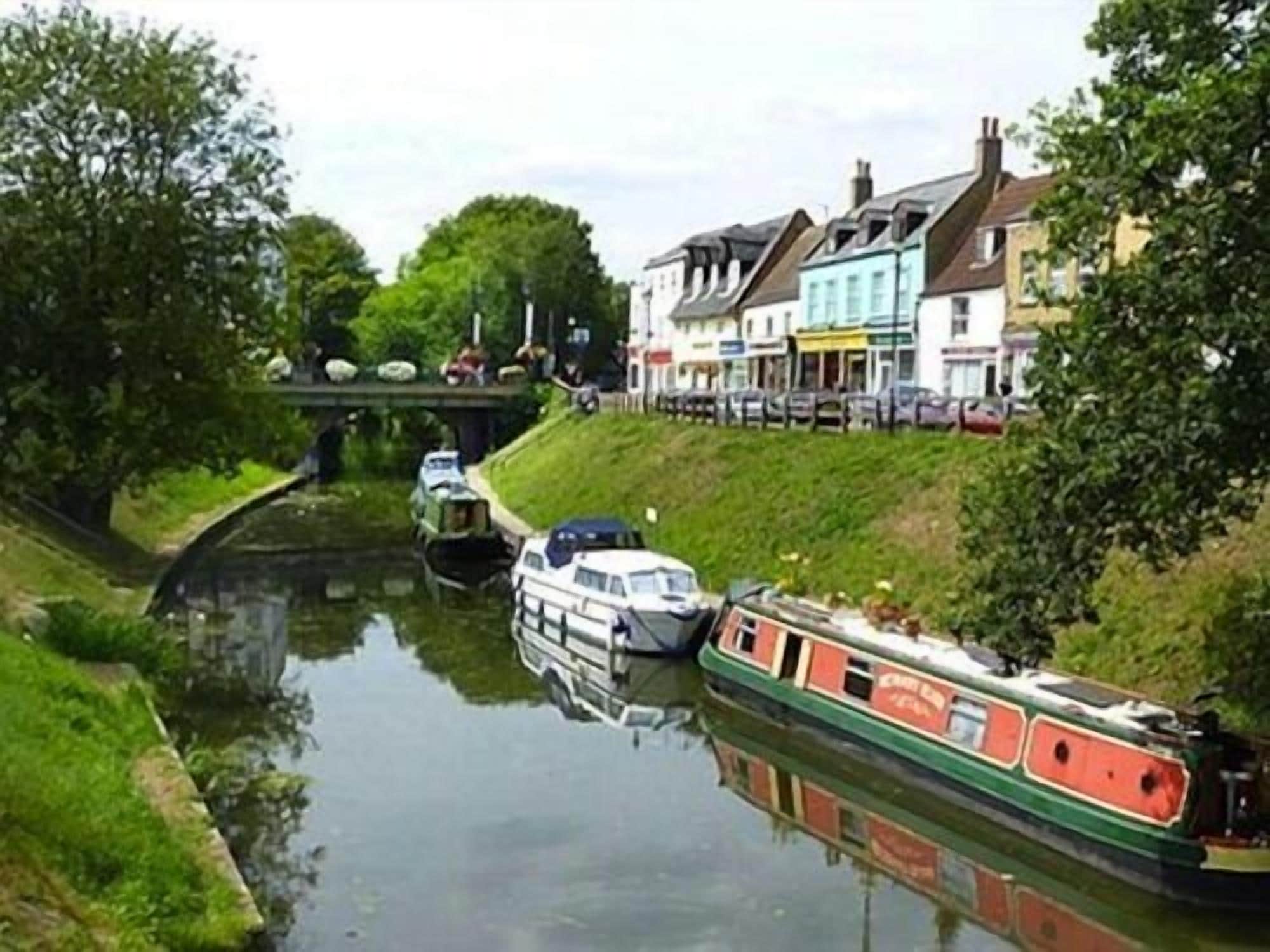 A narrow canal with boats, a bridge, and buildings along the banks.