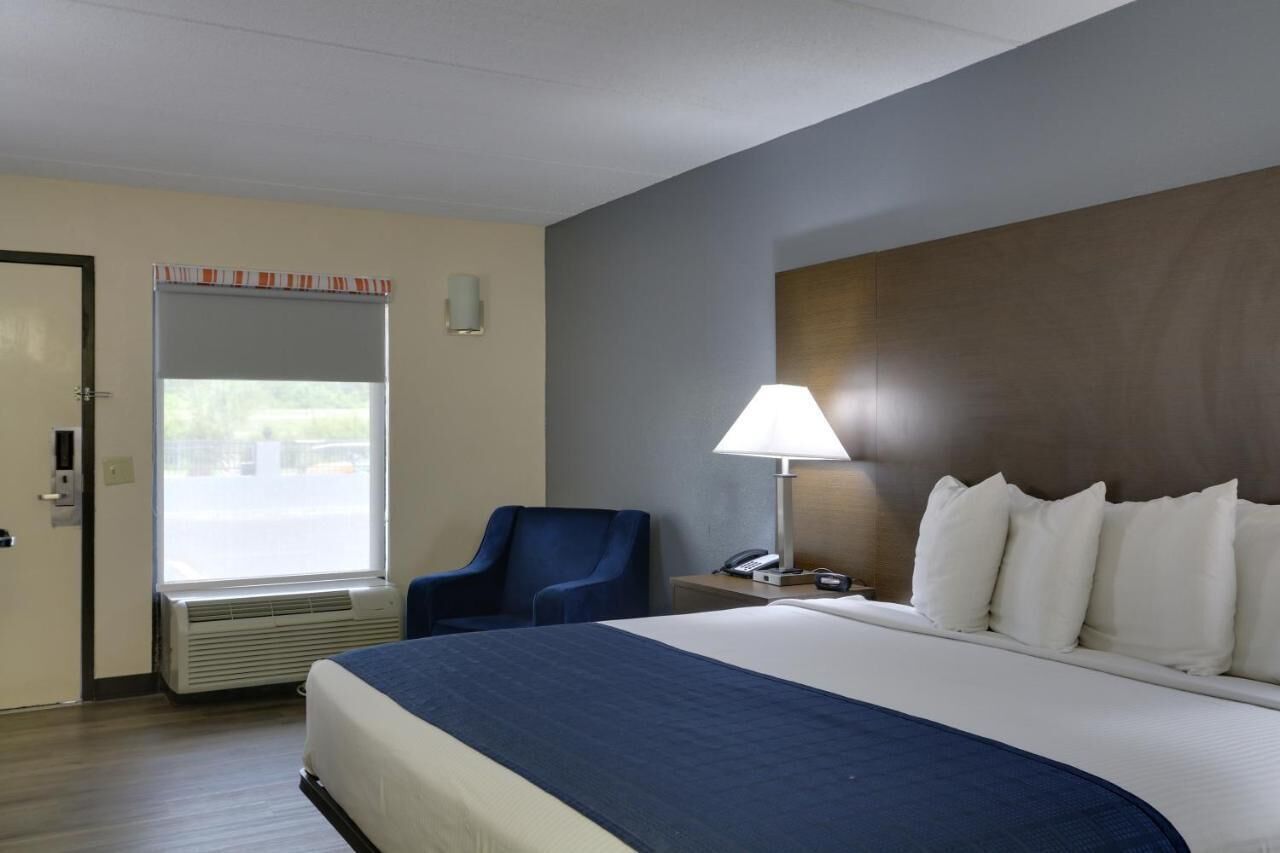 A hotel room with a large bed, a desk with a lamp, a chair, and a window with blinds.