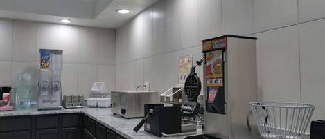 Una cucina accessoriata con macchina per il caffè, tostapane, piastra per waffle e frigorifero.