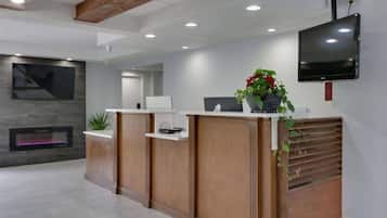 A reception area with wooden reception desks, a flat-screen TV mounted on the wall, a fireplace, and a potted plant.