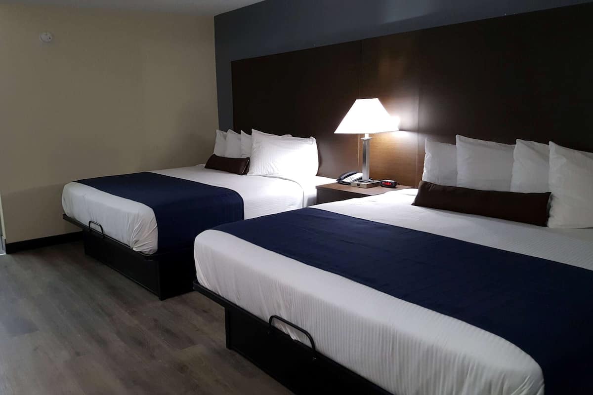 Two beds with white linens and dark blue bedspreads, a bedside table with a lamp, and a dark headboard.