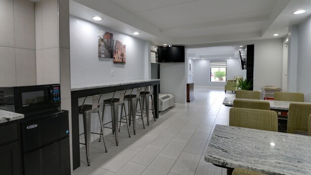 A modern kitchen with a built-in microwave, a refrigerator, and a bar area with stools. There is a dining area with tables and chairs. - Baymont by Wyndham Ridgeland I-95 (Ridgeland)