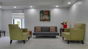 A modern living room with a grey sofa, two green armchairs, a red side table with a plant, and a painting on the wall. - Baymont by Wyndham Ridgeland I-95 (Ridgeland)