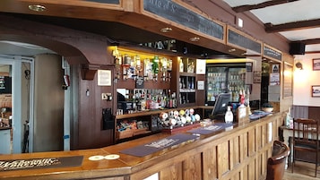 Una zona de bar con mostrador de madera, varias botellas y un menú en una pizarra.