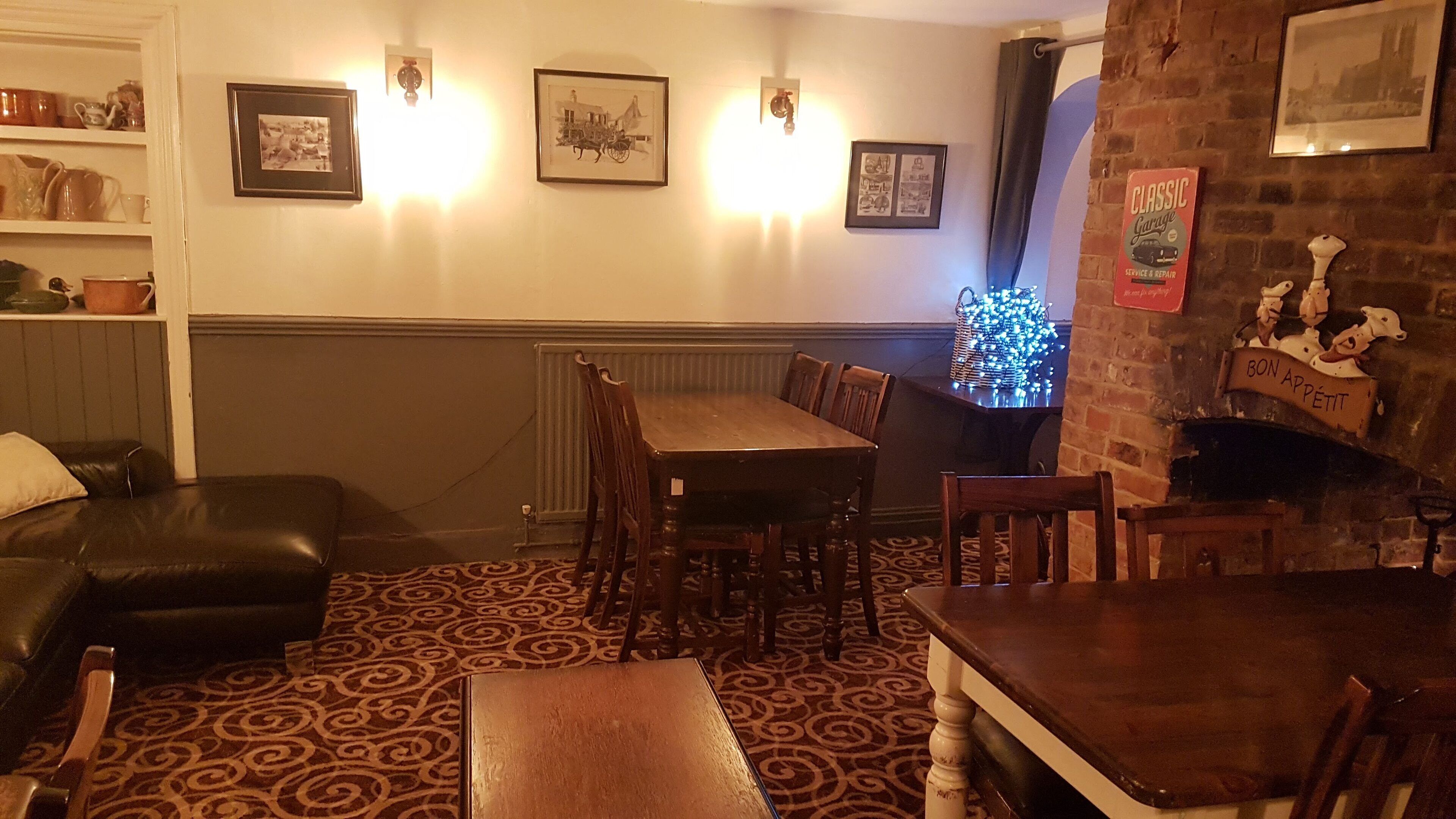 A cozy dining area with a wooden table and chairs, a patterned carpet, and a brick wall with a sign.