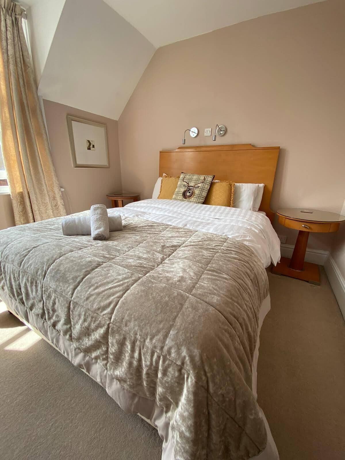 A neatly made bed with a quilted blanket, two bedside tables, and a clock on the wall.