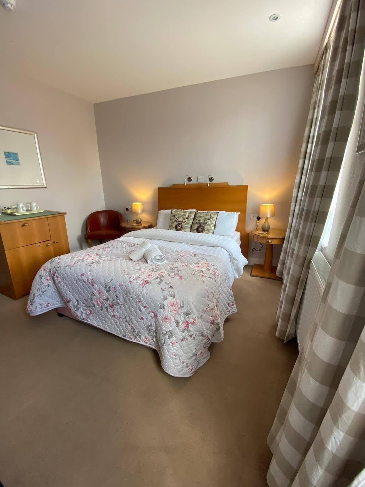 A hotel room with a large bed, a wooden dresser, a chair, and a nightstand with lamps.